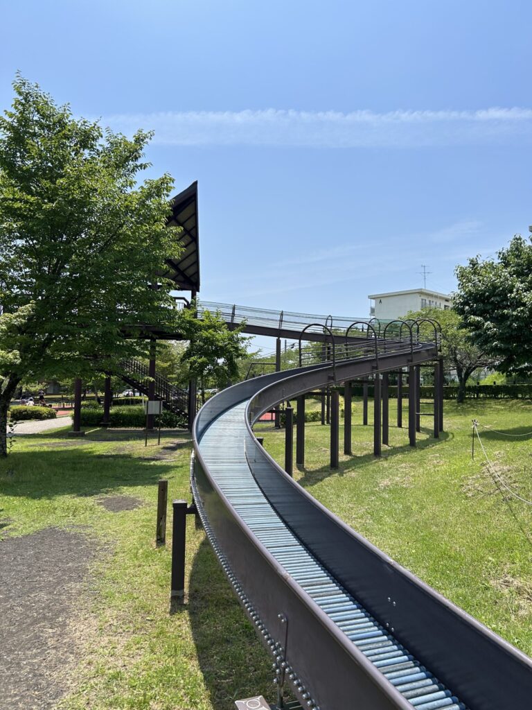 桜公園のローラーすべり台、周囲の緑と青空が広がる風景